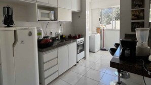 A kitchen with white cabinets, a microwave, a stove, and a refrigerator. - LK Santo Antônio 1 (Belo Horizonte)
