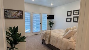 Un dormitorio con cama, televisor, puerta con persianas y una planta.