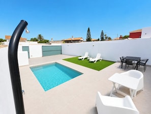 A rooftop pool with a small lawn area, white lounge chairs, and a table with chairs. - Essence Chiclana 1 . (Chiclana de la Frontera)