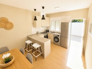 A compact kitchen with a central island, a washing machine, and a dining area with a table and chairs. - Essence Chiclana 1 . (Chiclana de la Frontera)