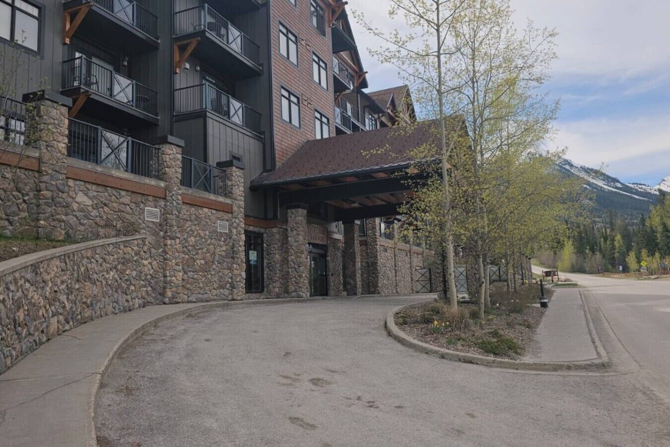 A multi-story building with stone and brick exterior, a covered entrance, and a mountain backdrop.