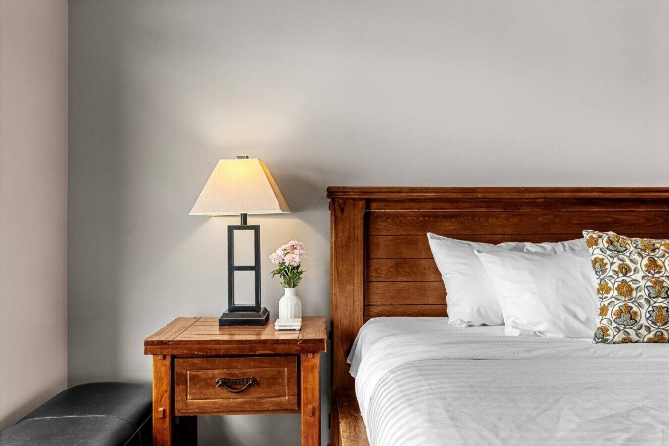 Een net opgemaakt bed met witte lakens, een houten hoofdbord en een kussen met een patroon.