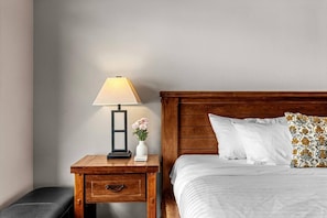Una cama bien hecha con sábanas blancas, cabecera de madera y un cojín estampado.