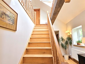 Eine Holztreppe mit Handlauf, ein gerahmtes Bild an der Wand, ein Blumentopf und ein Heizkörper.
