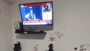 Keittiössä on televisio, joka on asennettu työtason yläpuolelle, kahvinkeitin ja kaksi baarijakkaraa.