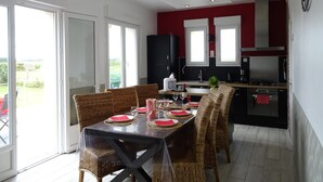 Un comedor con una mesa preparada para cuatro, una cocina con electrodomésticos modernos y un ventanal corredizo que da a un balcón.