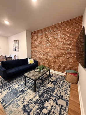 Ein Wohnzimmer mit Backsteinwand, einem dunkelblauen Sofa, einem Couchtisch und einem gemusterten Teppich.