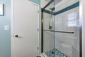 Een douche met glazen wanden, een metalen handgreep en een betegelde vloer.