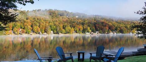 A lakeside view with Adirondack chairs, a fire pit, and a dock extending into the water.