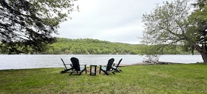 Uitzicht op een meer met twee Adirondack-stoelen en een kleintje tafeltje op een gazon.