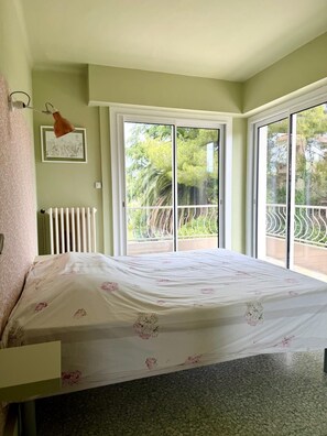 Ein Schlafzimmer mit Bett, Heizkörper, Fenster und Balkon.
