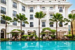 A hotel with a swimming pool, palm trees, and lounge chairs.