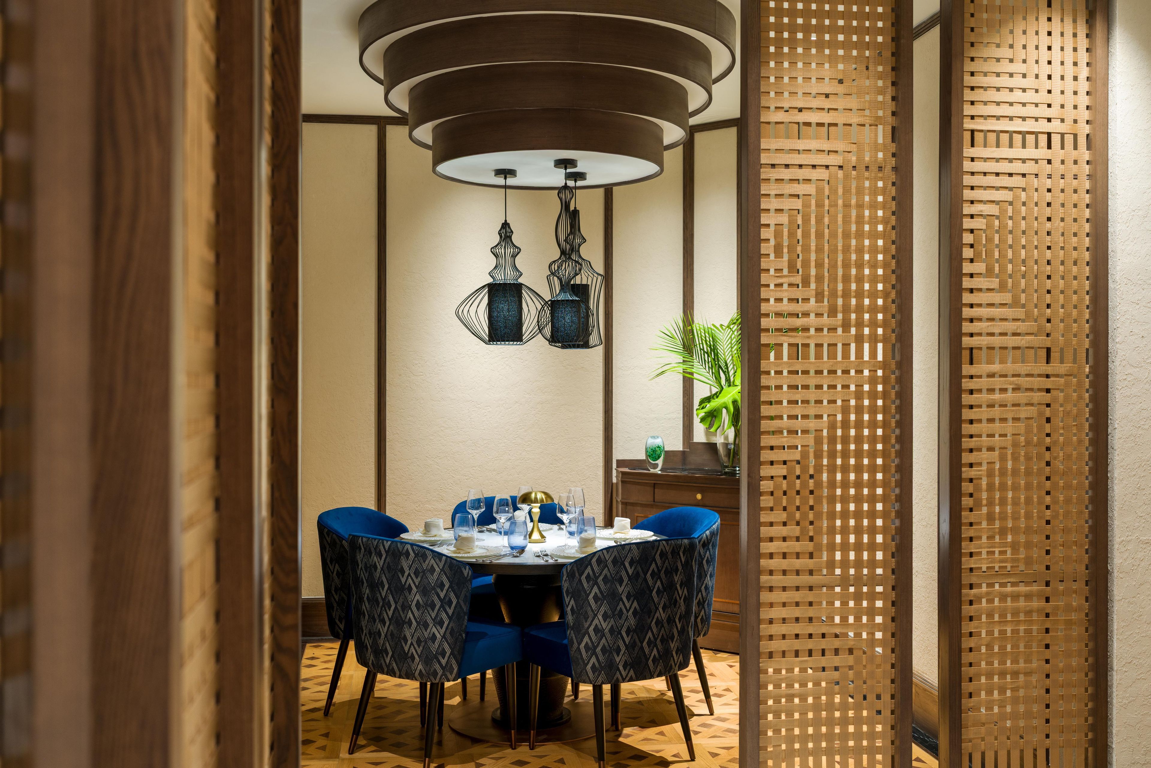 Comedor con una mesa redonda, sillas azules, una lámpara decorativa en el techo y un separador tejido.