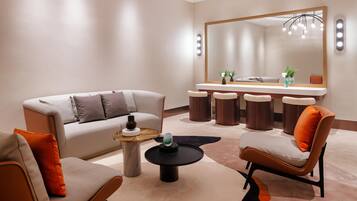 A modern living room with a sofa, armchairs, a coffee table, and a dining area with a mirror and stools.