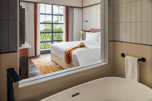 Ett hotellrum med en stor säng, ett badrum med badkar och utsikt över grönområden utanför.
