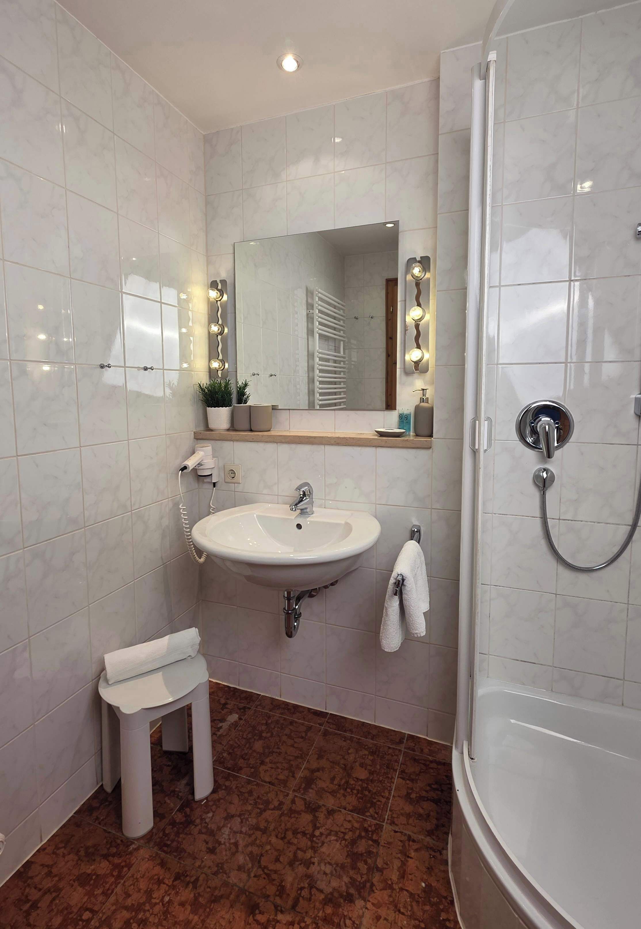 Un baño con lavamanos, espejo, toallero y ducha.