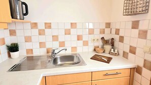 Een kleine keuken met een roestvrijstalen spoelbak, houten kastjes, een wit aanrechtblad en een spatwand met een ruitmotief.