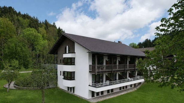 Een modern, tweelaags gebouw met een balkon, omringd door een verzorgd gazon en bomen.