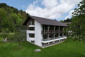 Ein modernes, zweistöckiges Gebäude mit Balkon, umgeben von einem gepflegten Rasen und Bäumen.