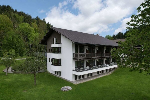 Ein modernes, zweistöckiges Gebäude mit Balkon, umgeben von einem gepflegten Rasen und Bäumen.