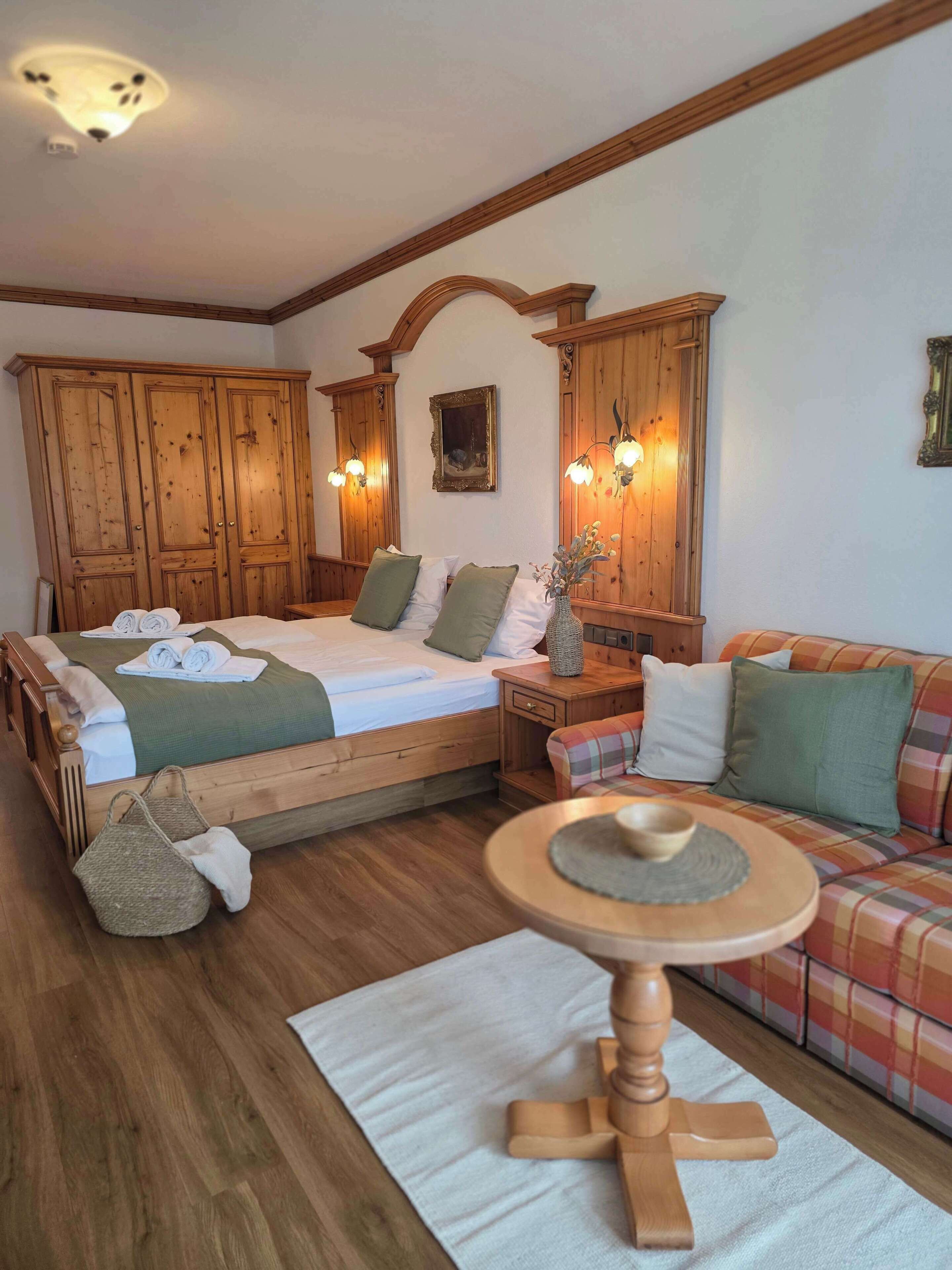 A bedroom with a wooden bed, a wooden nightstand, a plaid sofa, and a wooden table.