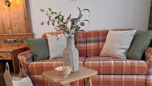 Een gezellige woonkamer met een geruite bank, een geweven vaas met planten, een houten tafel en een geweven poef.