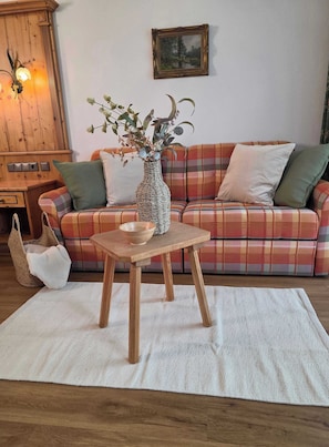 Ein gemütliches Wohnzimmer mit einem karierten Sofa, einer gewebten Vase mit Pflanzen, einem Holztisch und einem gewebten Pouf.