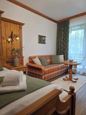 Ein Zimmer mit einem Bett, einem Sofa, einem Holzschrank, einem Tisch und einem Fenster mit Vorhängen.