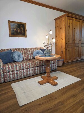 Una sala de estar con un sofá estampado, una mesa redonda de madera con un florero, y un mueble grande de madera.