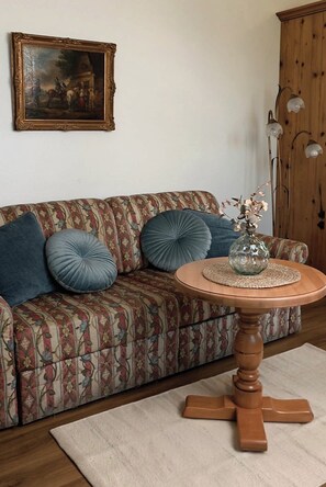 Un salon avec un canapé à motifs, une table ronde en bois et un tableau encadré accroché au mur.