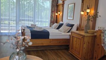 A bedroom with a wooden bed, a nightstand, a vase with flowers, and a window with sheer curtains.
