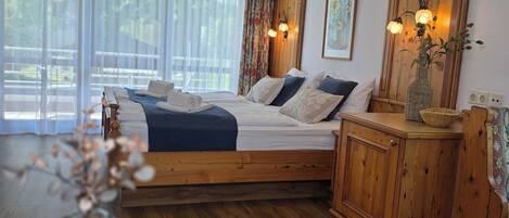 Un dormitorio con una cama de madera, una mesita de noche, un florero con flores y una ventana con cortinas ligeras.