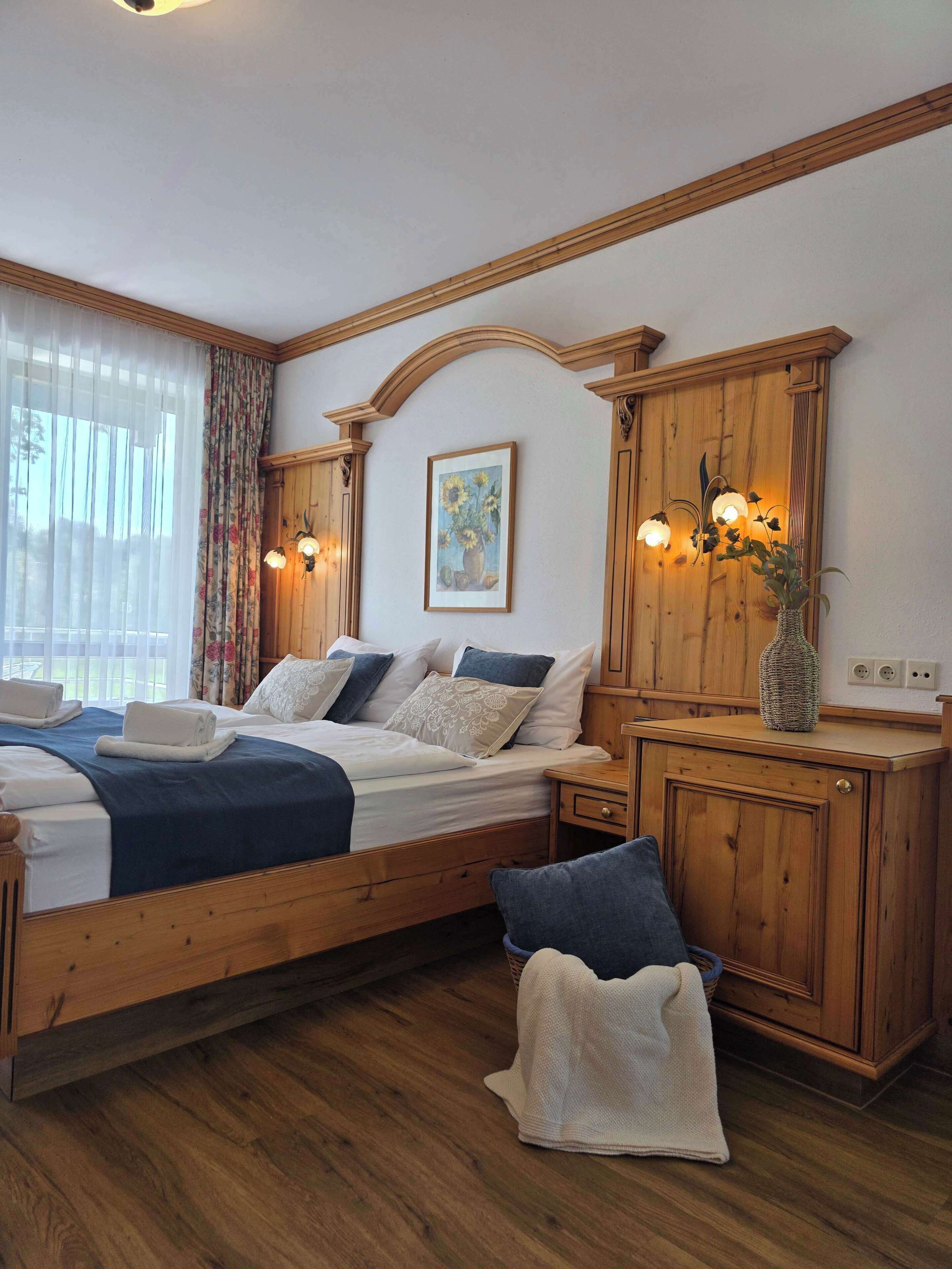 A bedroom with a wooden bed, a nightstand, a dresser, and a painting on the wall.
