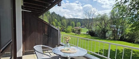 Un balcón con mesa y sillas, vistas a un paisaje verde y techo de madera.
