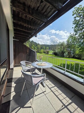 A balcony with a table and chairs, a view of a green landscape, and a wooden ceiling.