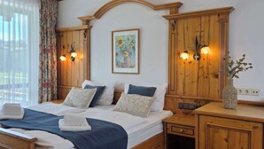 A wooden-framed bed with a headboard, two bedside tables with lamps, a floral curtain, and a painting of sunflowers. - Alpine Retreat: Pet-Friendly Apartment w/ Free (Fischbachau)