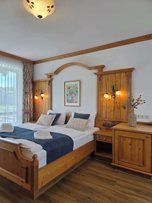 Un lit en bois avec une tête de lit, deux tables de chevet avec des lampes, un rideau à motifs floraux et un tableau représentant des tournesols.