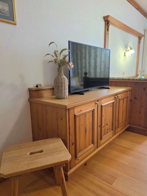 Ein Holzkabinett mit einem Fernseher darauf, einem kleinen Tisch und einer Blumenvase.