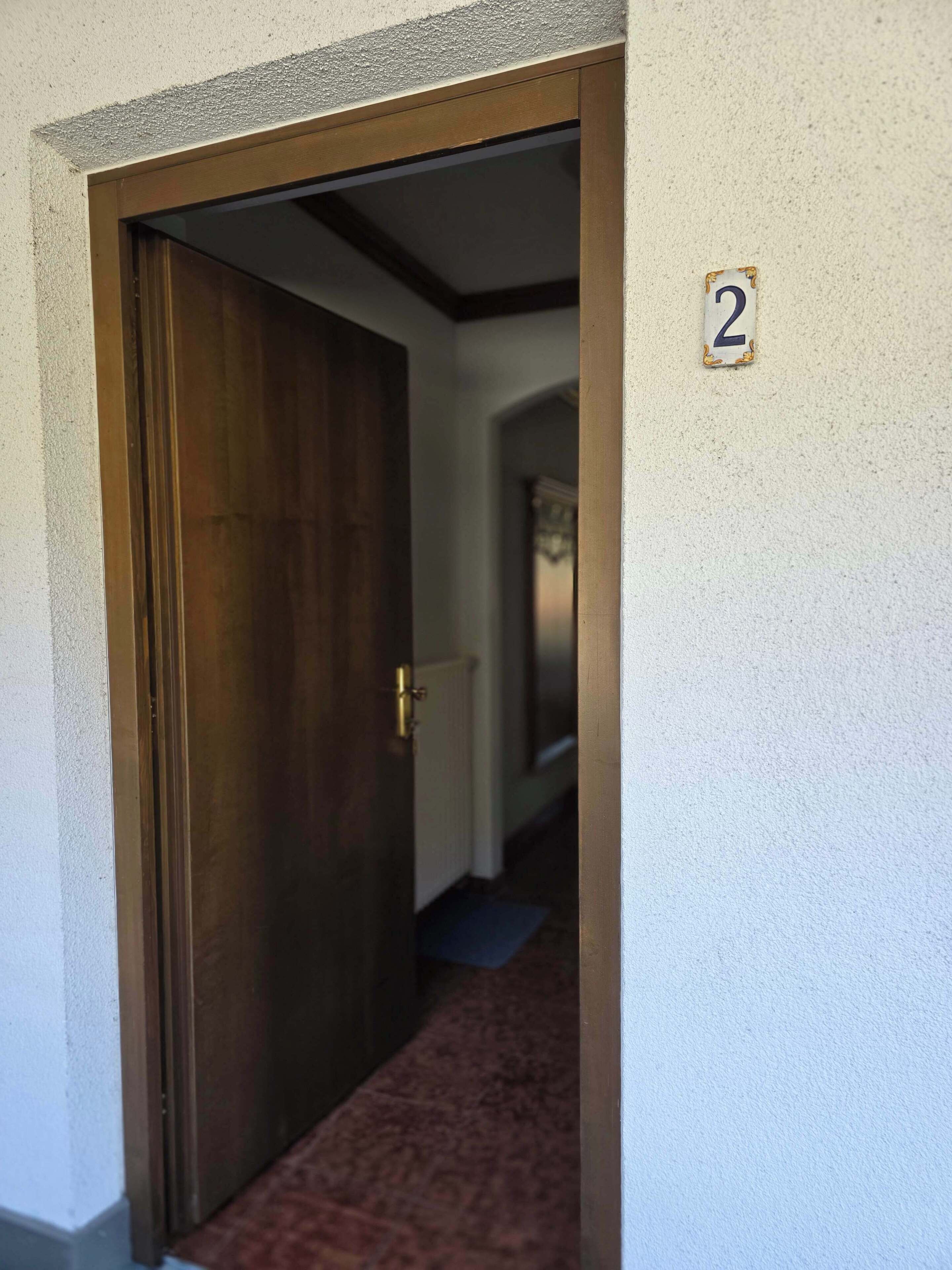 A hallway with a wooden door, a carpeted floor, and a number '2' sign on the wall.