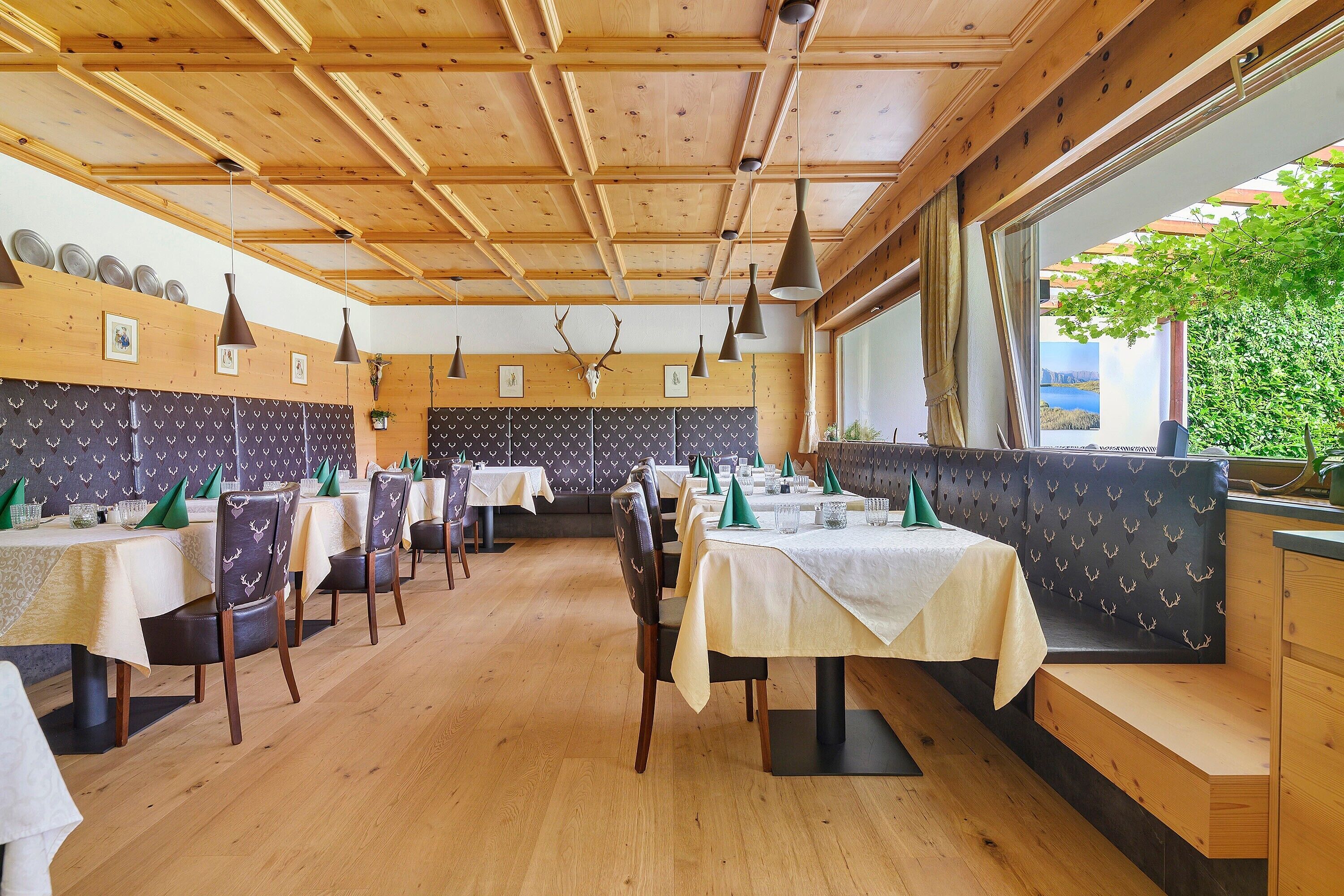 Un restaurante con vigas de madera en el techo, mesas con manteles blancos y un amplio ventanal con vistas.