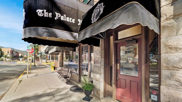 A building with a black awning labeled 'The Palace Hotel,' a red door, and a potted plant outside. - Downtown Palace Hotel Suite - Steps to Adventure (Salida)