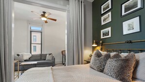 A bedroom with a bed, a ceiling fan, a window, a sofa, and framed pictures on the wall. - Downtown Palace Hotel Suite - Steps to Adventure (Salida)