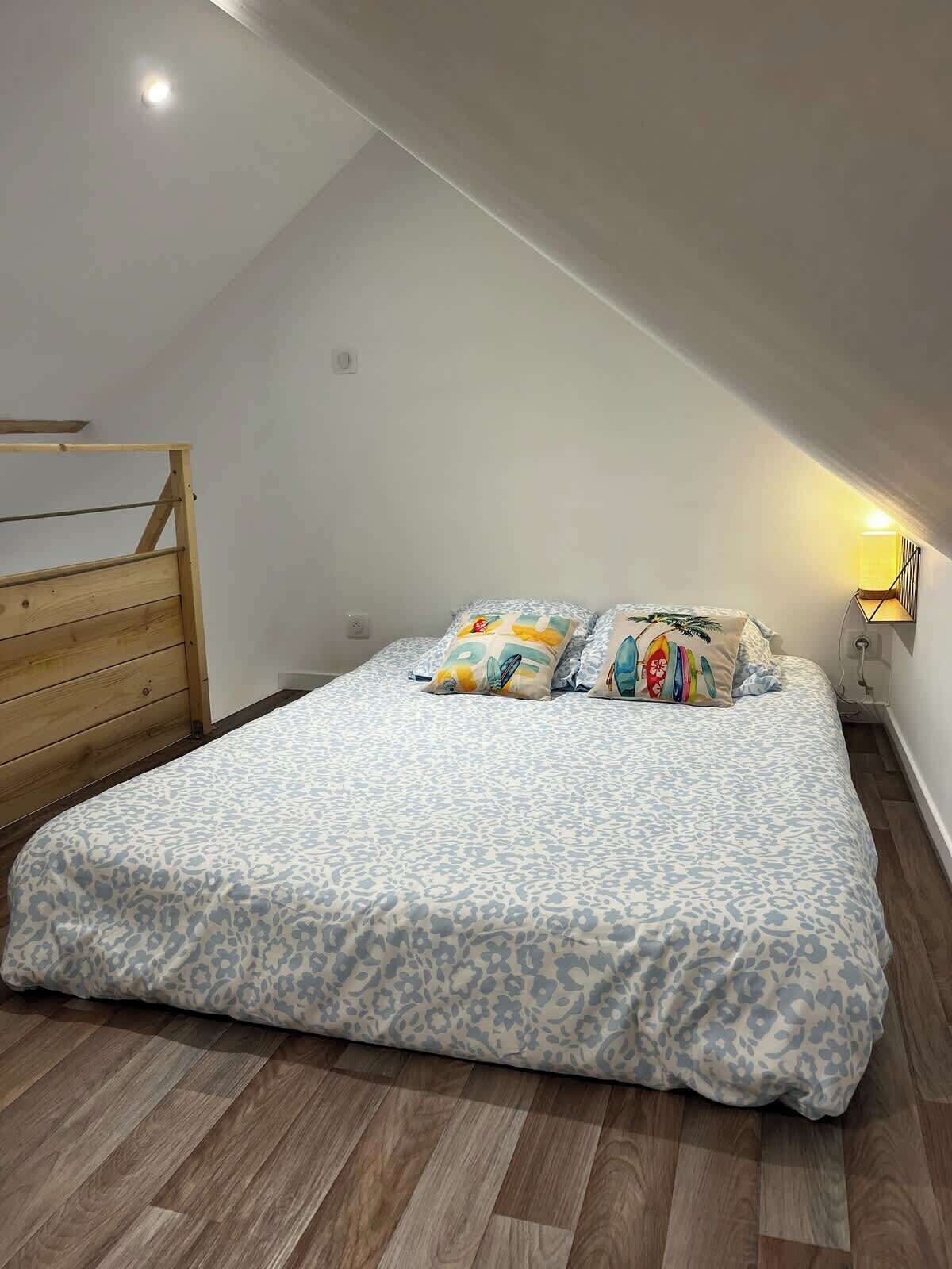 Une chambre avec un plafond en pente, une tête de lit en bois, un lit avec une literie à motifs et une lampe de chevet.