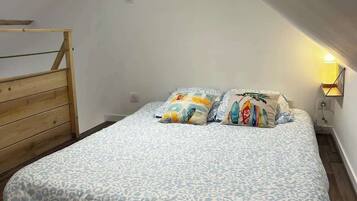 Une chambre avec un plafond en pente, une tête de lit en bois, un lit avec une literie à motifs et une lampe de chevet.