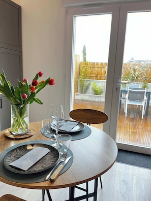 Une table à manger dressée avec des assiettes, des couverts et un vase de tulipes.