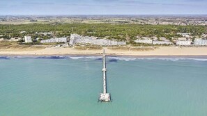 An aerial view of a coastal area with a long pier extending into the water, surrounded by buildings and a beach.