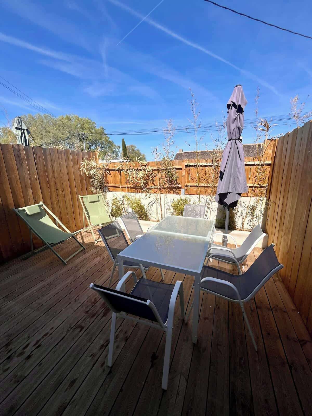 A wooden deck with a glass table and metal chairs, surrounded by a wooden fence.
