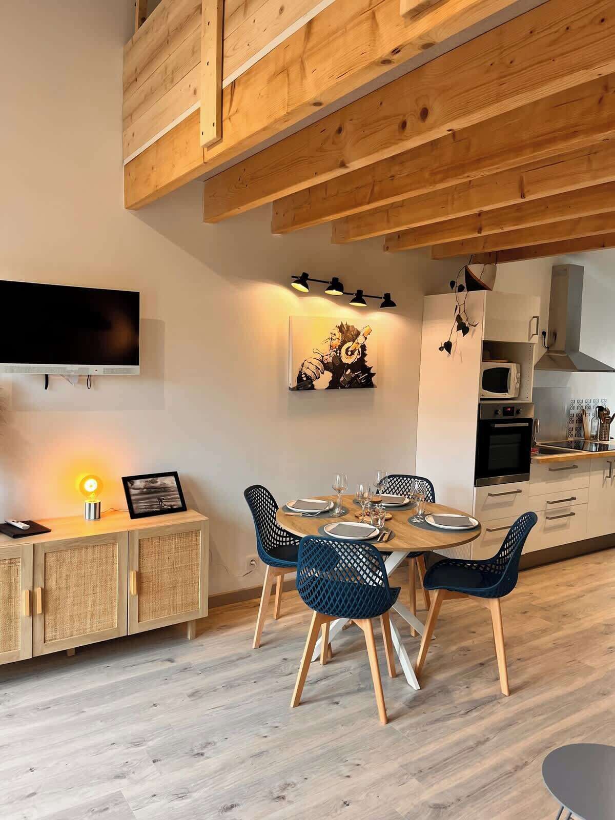 Une cuisine moderne avec des poutres en bois, une table à manger pour quatre personnes et un téléviseur fixé au mur.