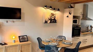 Une cuisine moderne avec des poutres en bois, une table à manger pour quatre personnes et un téléviseur fixé au mur.
