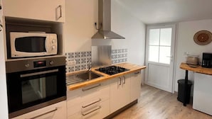 A modern kitchen with a microwave, oven, gas stove, and a stainless steel range hood. - 2/ Pavillon neuf proche plage (Saint-Jean-de-Monts)